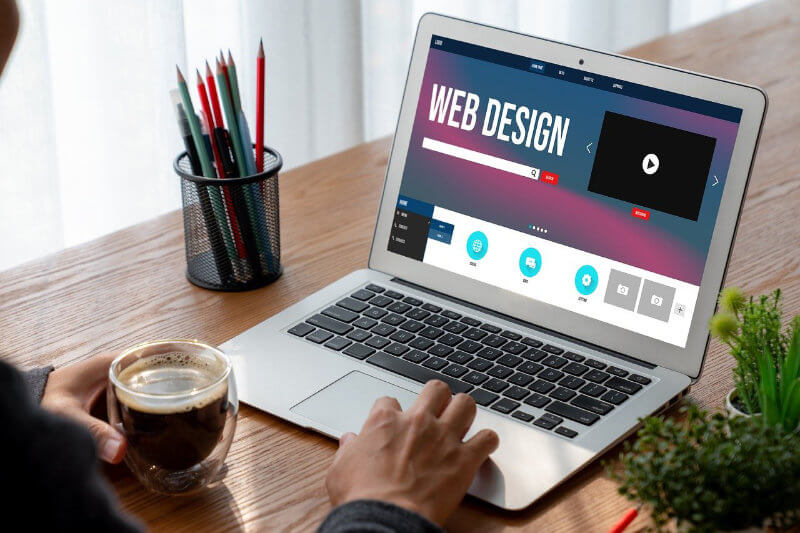 Website Design Company working on building a website on a laptop with a cup of coffee in their hand